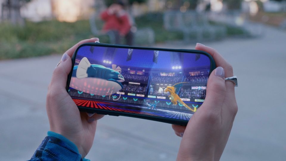 Hands holding mobile device, on-screen is a match between Charizard and Hisuian Samurott versus Dondogo and Aegislash.